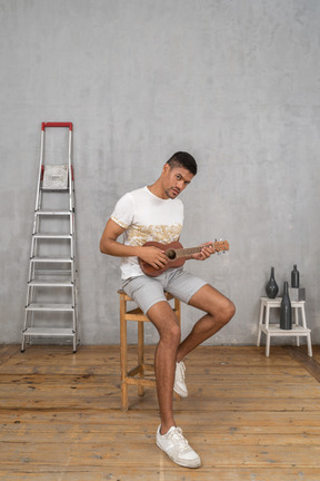 Three-quarter view of a man posing with ukulele on a stool
