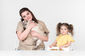 Mamma seduta accanto a una figlia nella sedia per bambini e in possesso di un gatto