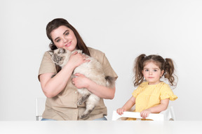 Mamá sentada junto a una hija en la silla de los niños y sosteniendo un gato