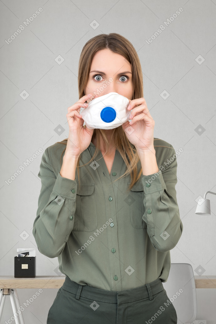 A surprised looking woman putting on a face mask