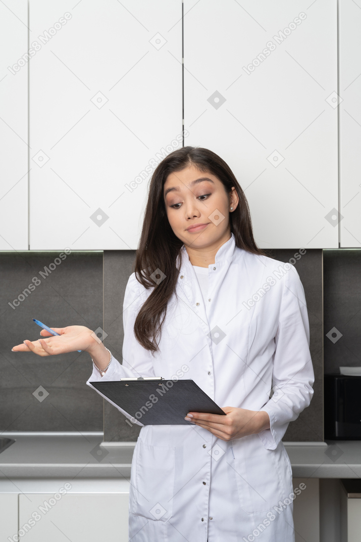 Front view of a puzzled female doctor holding a pen and looking down the tablet