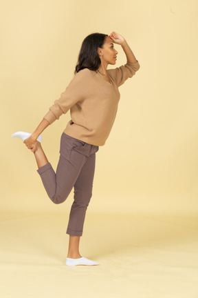 Vista lateral de una mujer joven de piel oscura tocando su pierna y tobillo