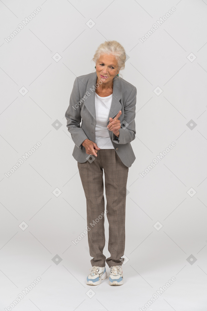 Vista frontal de una anciana en traje agachándose y mostrando una señal de advertencia