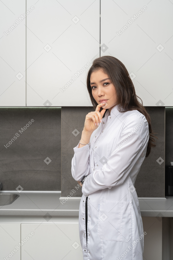 Vista de três quartos de uma médica tocando os lábios e olhando para a câmera