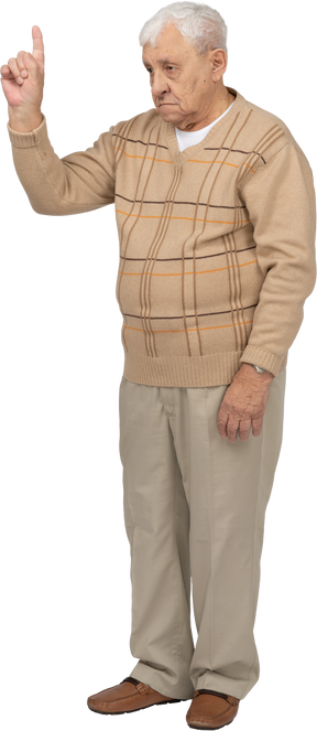 Vista frontal de un anciano con ropa informal apuntando hacia arriba con un dedo