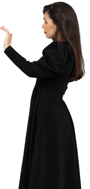 Vue latérale d'une jeune femme vêtue d'une robe noire levant la main