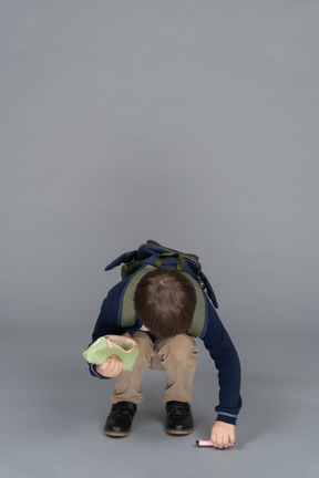 Little boy crouching down to pick up a pen