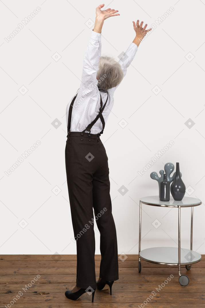 Three-quarter back view of an old lady in office clothing raising her hands