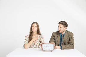 Couple sitting at the table and holding a clock