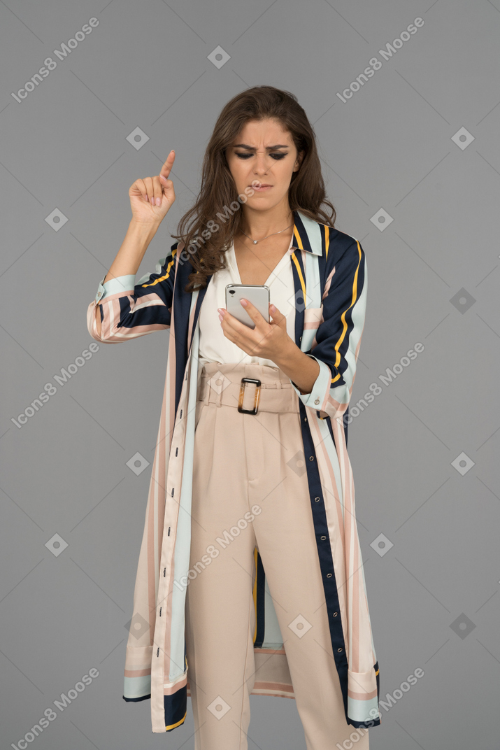 Anxious young woman pointing up with finger and looking at mobile phone