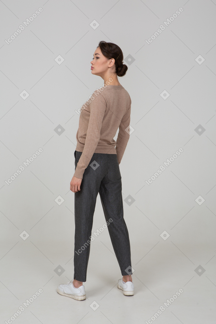 Vista posterior de tres cuartos de una señorita parada quieta en suéter y pantalones mirando a un lado
