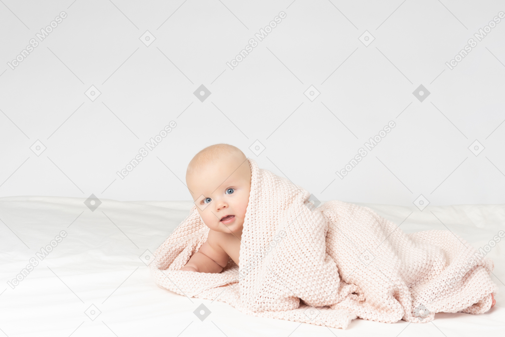Smiling baby boy covered in beige knitted blanket