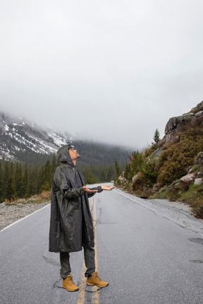 A man in a raincoat walking on the side of a road