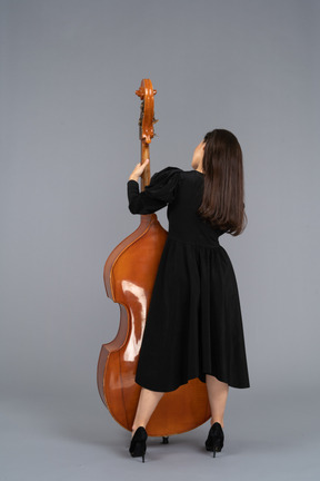 Vista de trás de uma jovem musicista vestida de preto segurando seu contrabaixo