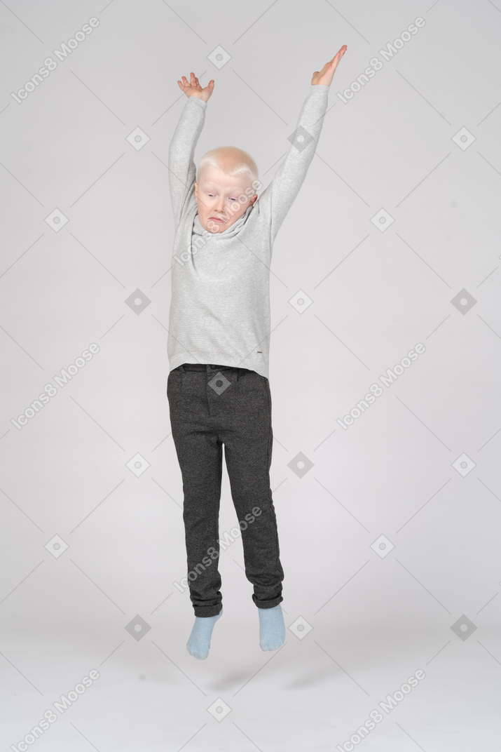 Front view of a young boy jumping with hands up in the air