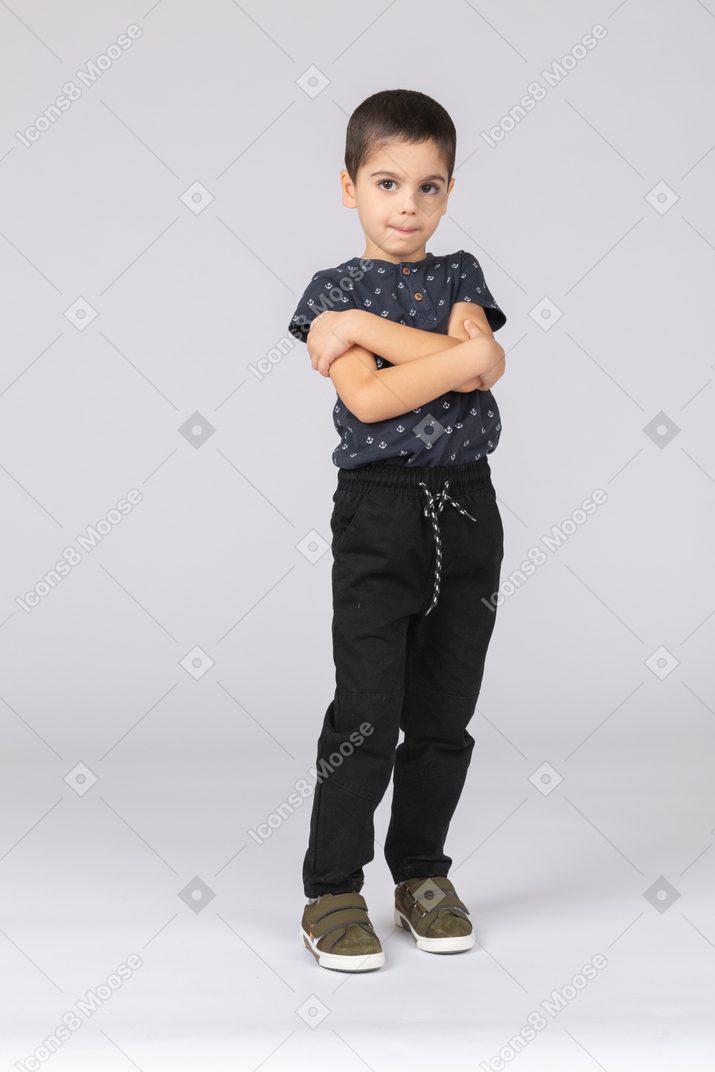 一个可爱的男孩交叉双臂摆姿势，看着相机的前视图