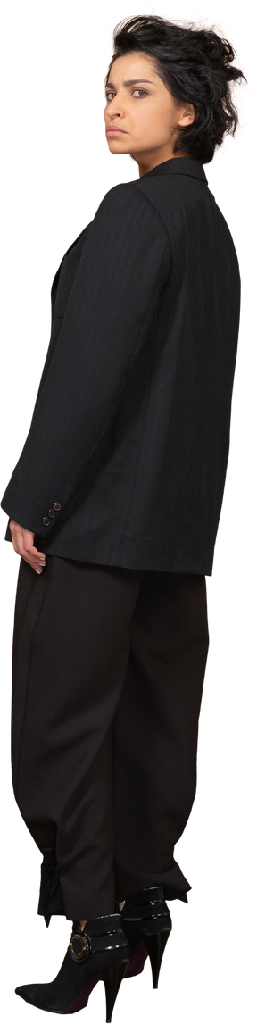 Vista posteriore di tre quarti di una donna d'affari scontenta in un abito nero, guardando la fotocamera
