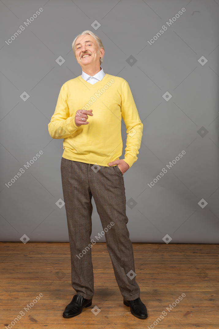 Вид спереди довольного улыбающегося старика в желтом пуловере, поднимающего руку и смотрящего в камеру