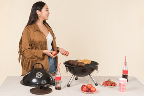 Young asian woman standing near grill and holding fruits