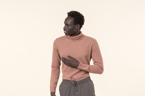 Un jeune homme noir dans un col roulé beige et un pantalon de jogging gris se tenant par hasard sur le fond blanc