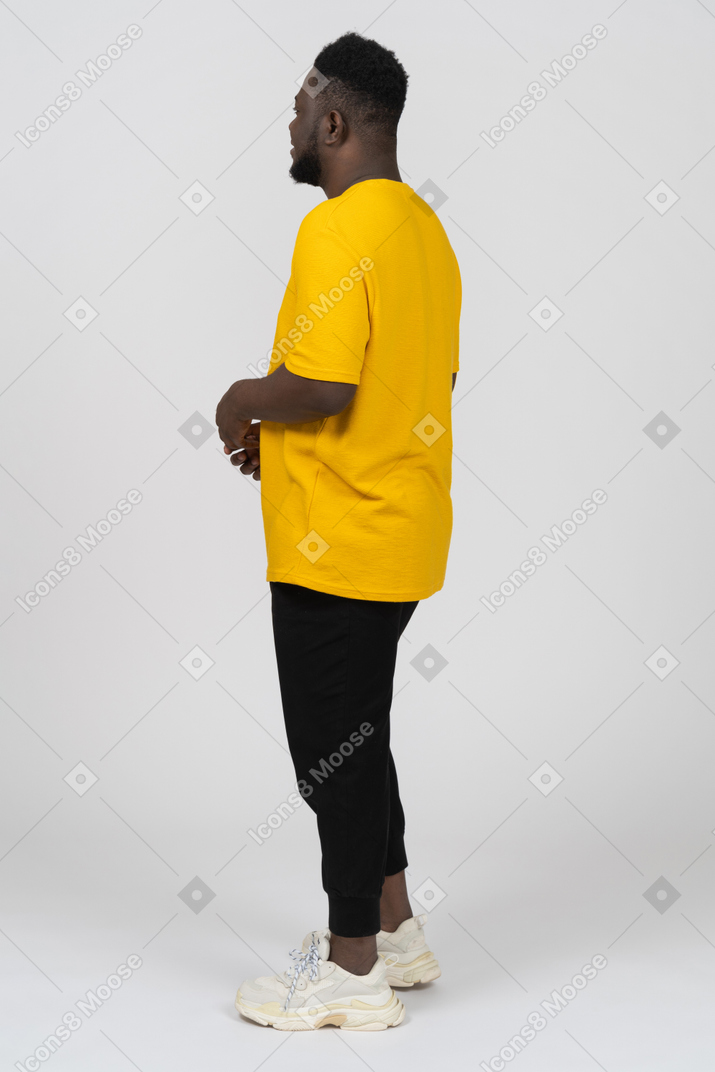 Three-quarter back view of a young dark-skinned man in yellow t-shirt holding hands together