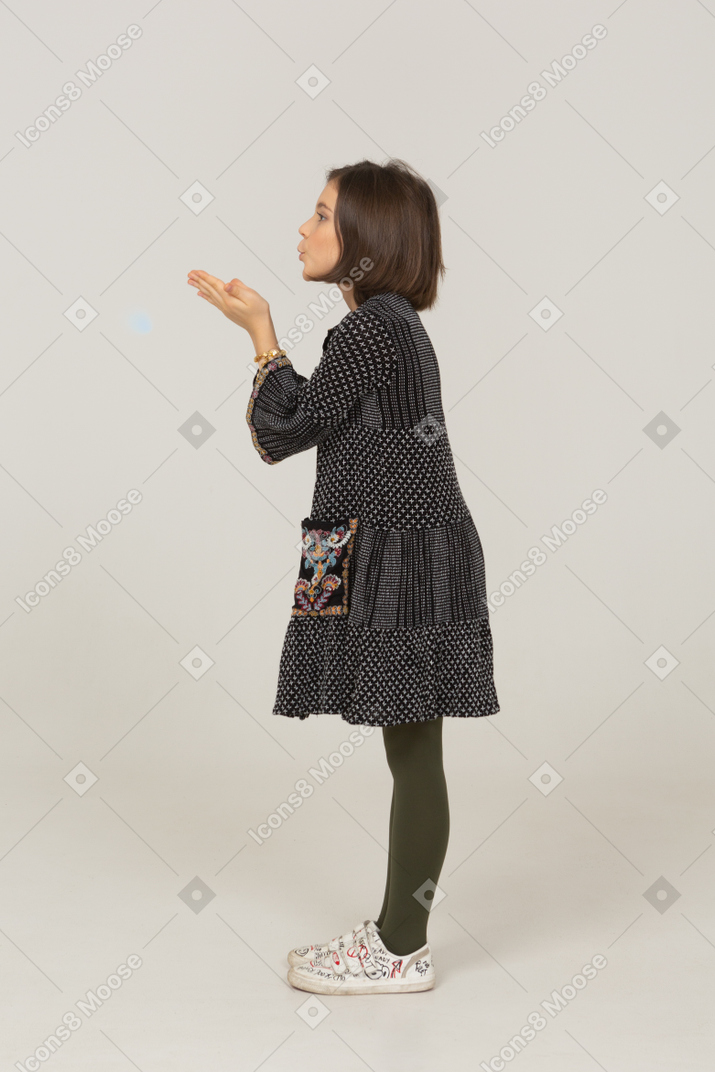 Vista lateral de una niña vestida enviando un beso al aire