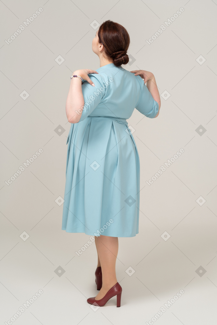 Rear view of a woman in blue dress posing with hands on shoulders