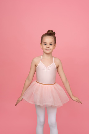 可爱的小芭蕾舞演员站在她的手放在一边