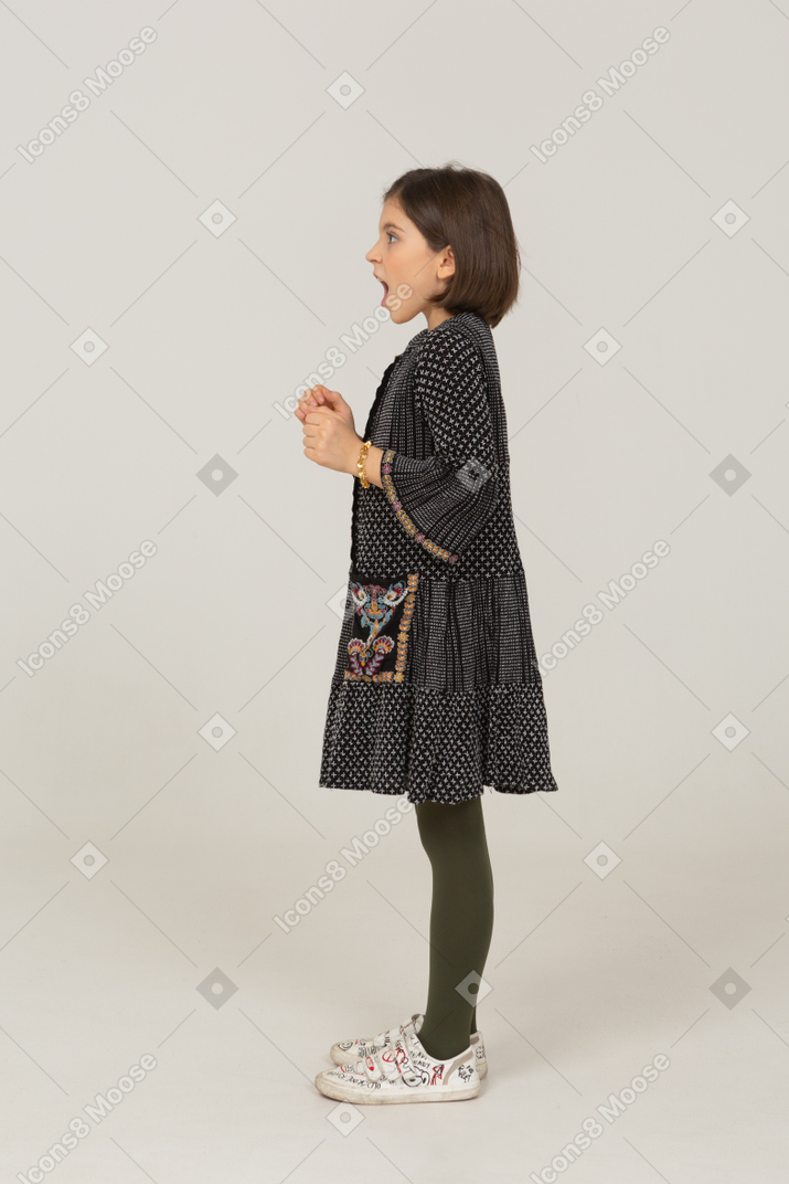 Vista laterale di una bambina eccitata in abito stringendo i pugni