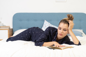 Vista frontale di una giovane donna annoiata che legge un libro a letto