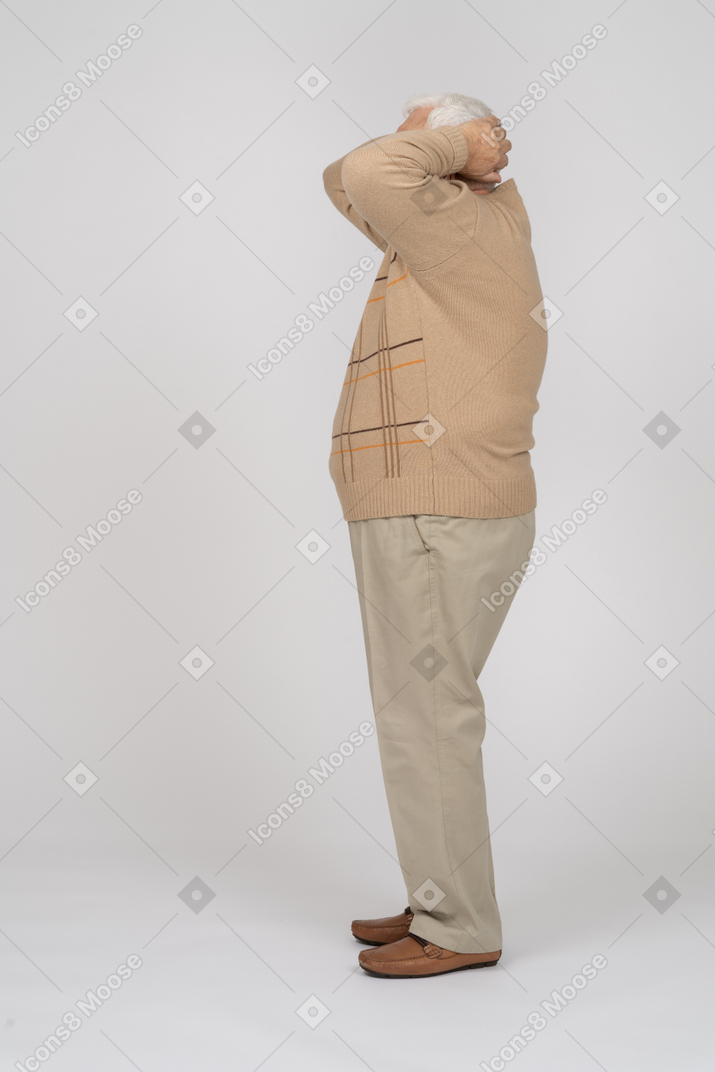頭の後ろに手を置いて立っているカジュアルな服装の老人の側面図