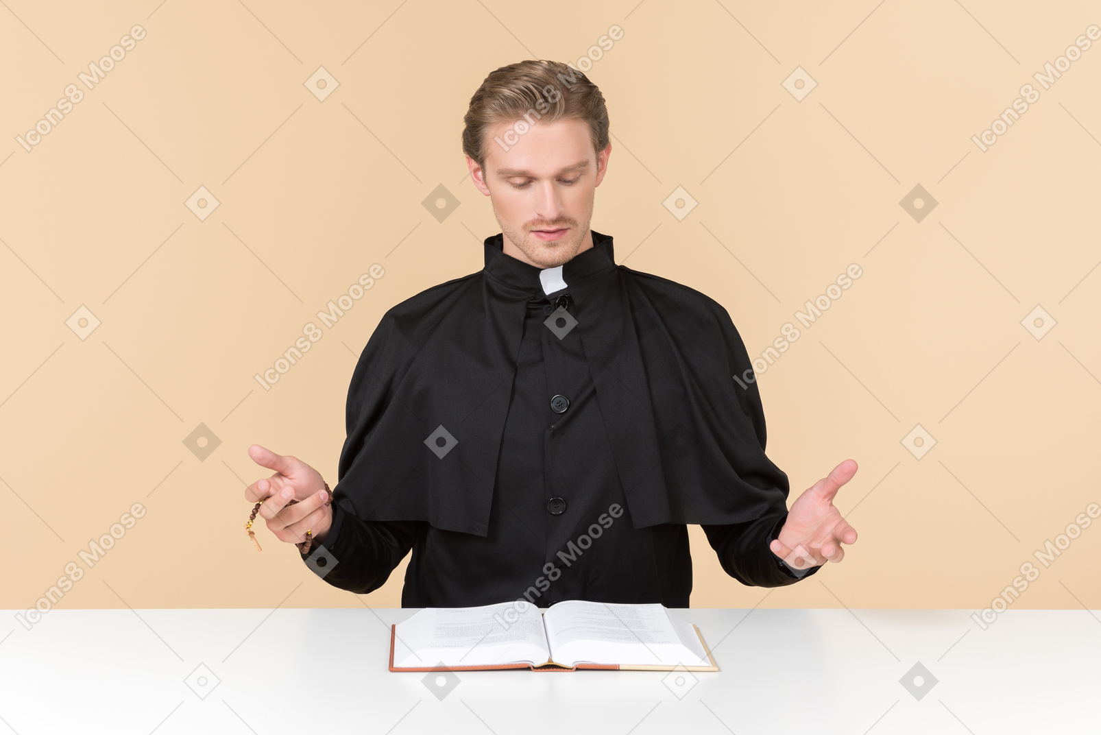 가톨릭 신부가 오픈 성경 책과 함께 테이블에 앉아 무언가를 말하는 것을 좋아합니다.