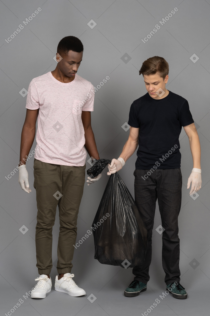 Двое молодых людей поднимают черный мешок для мусора