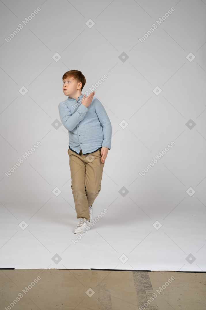 A boy standing and gesturing at something at his side