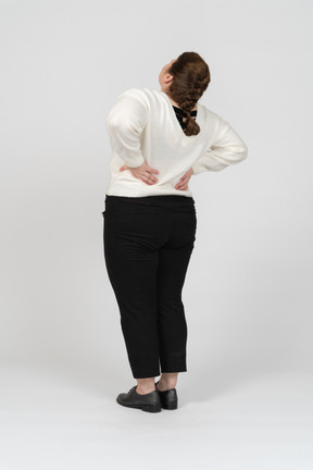 Retrovisor de uma mulher gorducha de suéter branco, sofrendo de dores na região lombar