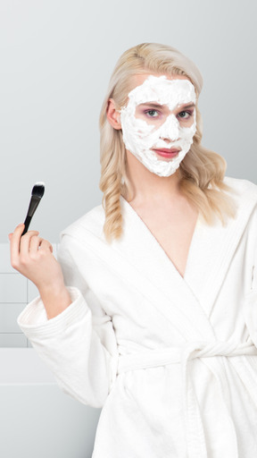 A young woman in a white bathrobe with a facial mask on her face
