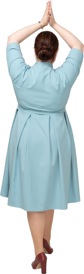 祈りのジェスチャーを作る青いドレスを着た女性の背面図