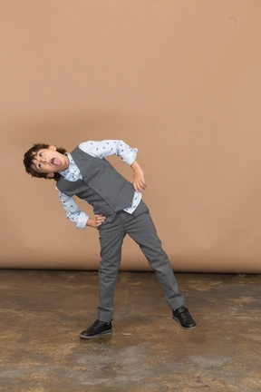Front view of a boy in suit posing with hands on hips and showing tongue