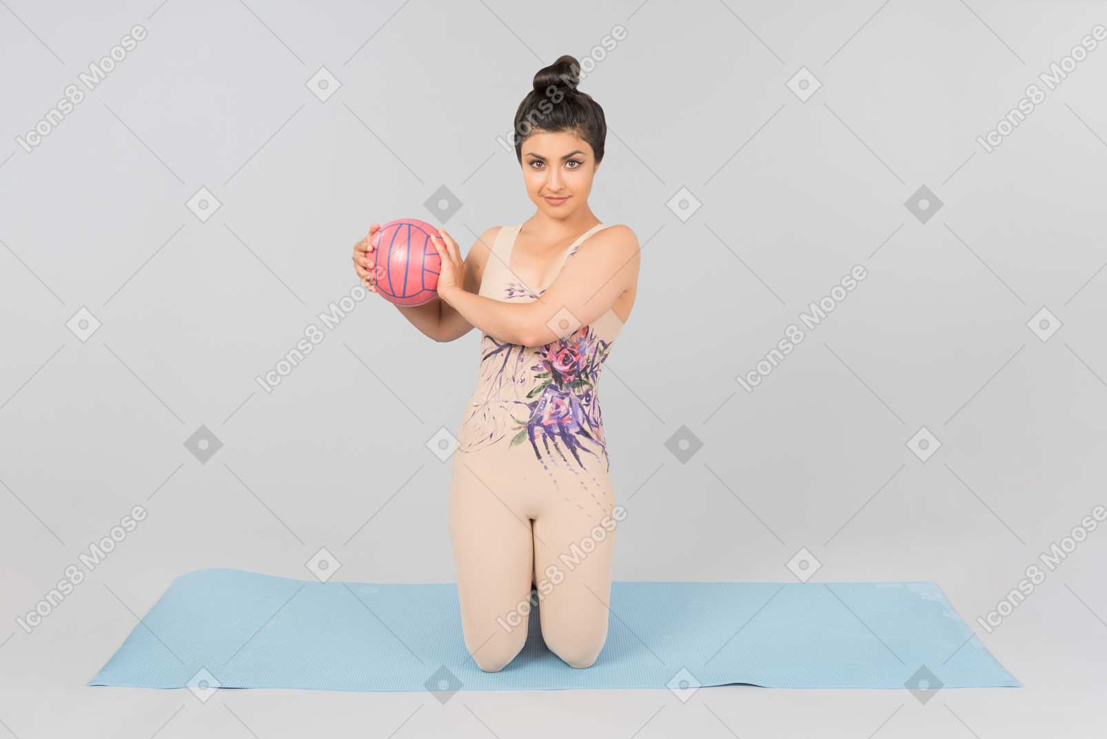 Joven gimnasta india sentada sobre una estera de yoga y sosteniendo la pelota con ambas manos