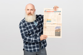 Bearded man showing a newspaper while looking alarmed