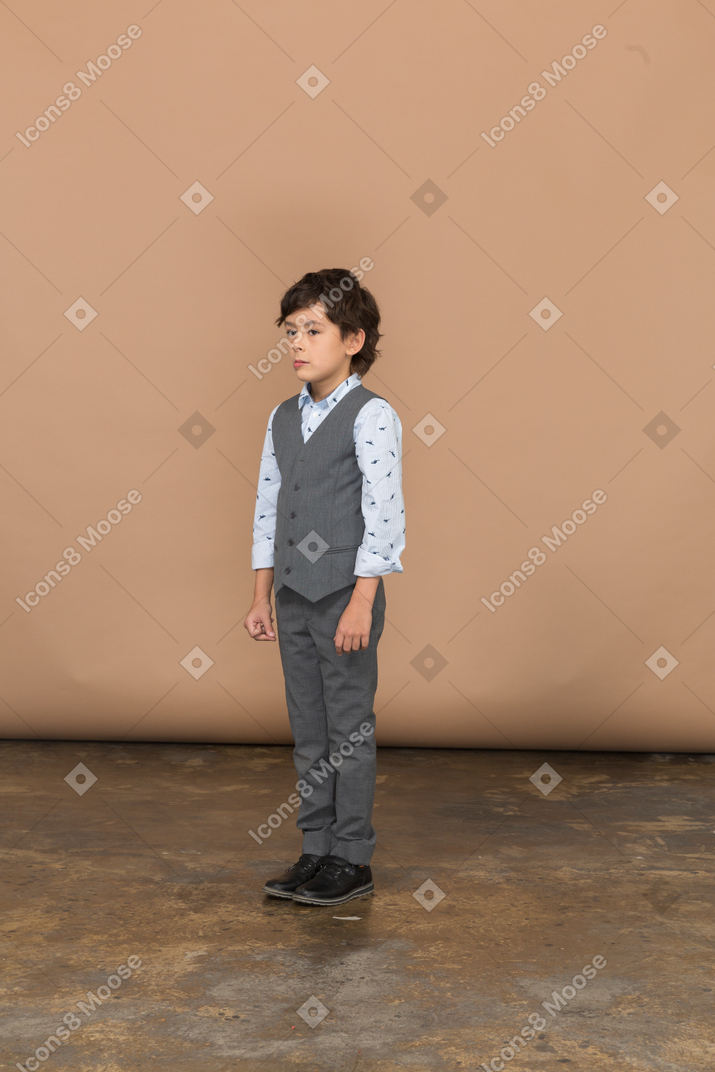 Vista frontal de um menino sério de terno cinza parado