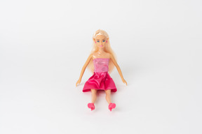 Una hermosa muñeca barbie en un vestido rosa brillante y zapatos de tacón rosa sentado aislado contra un fondo blanco liso