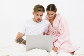 Casal sentado na cama e trabalhando no laptop