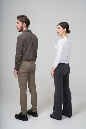 Vista de tres cuartos de una pareja joven en ropa de oficina mostrando la lengua