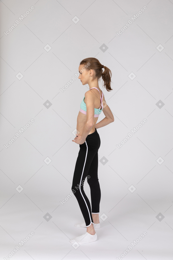 Vista lateral de una jovencita en ropa deportiva poniendo las manos en las caderas