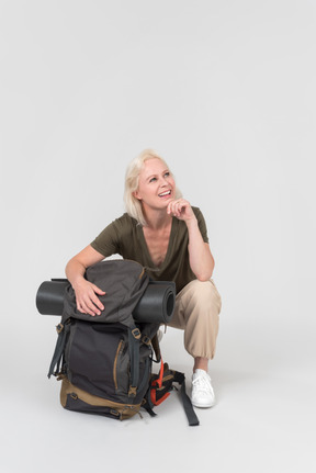 Laughing mature female tourist sitting near backpack