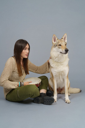 De cuerpo entero de una maestra sosteniendo un tambor y sentada con su perro