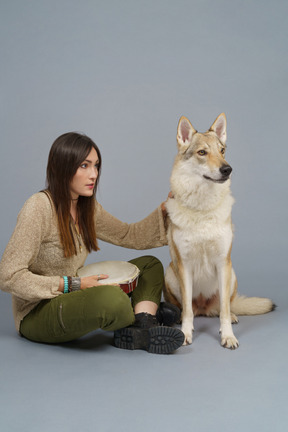 Comprimento total de uma dona segurando um tambor e sentada com seu cachorro