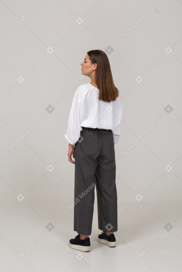 Vista posterior de tres cuartos de una joven disgustada en ropa de oficina mirando a un lado