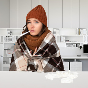 A sick woman is sitting with thermometer in mouth